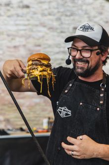 Beefy Boys co-founder Murf proudly holds up a stacked cheeseburger with dripping sauce.