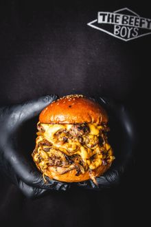 A Beefy Boys smashed patty burger held in a gloved hand.