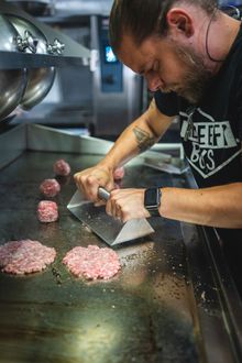 A Beefy Boys chef pressing one of their signature smashed beef patties on a grill.