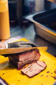 Slicing cooked meat on a yellow cutting board - Beefy Boys BBQ Nights 2025 Slicing cooked meat on a yellow cutting board - Beefy Boys BBQ Nights 2025